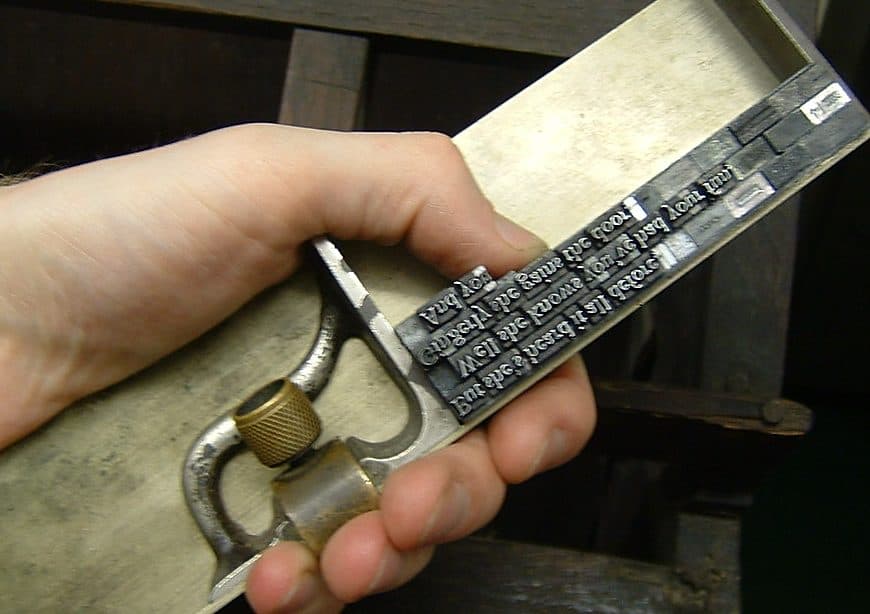 A hand holding a metal composing stick filled with set type.