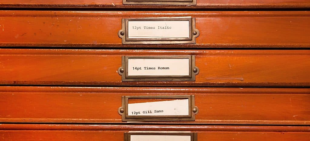 Row of labelled letterpress type-case drawers in a wooden cabinet.